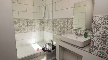 Baño con ducha, inodoro, lavabo y espejo.