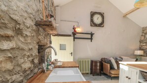 A rustic kitchen with a stone wall, wooden flooring, a sink, a clock, and a cozy seating area. - The Cottage at Thorpe Farm (York)