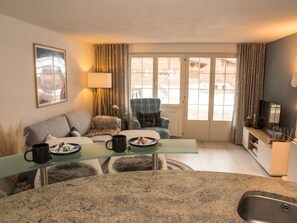 Ein modernes Wohnzimmer mit einem Glastisch, einer Couch, einem Sessel und einem Essbereich mit Spüle.