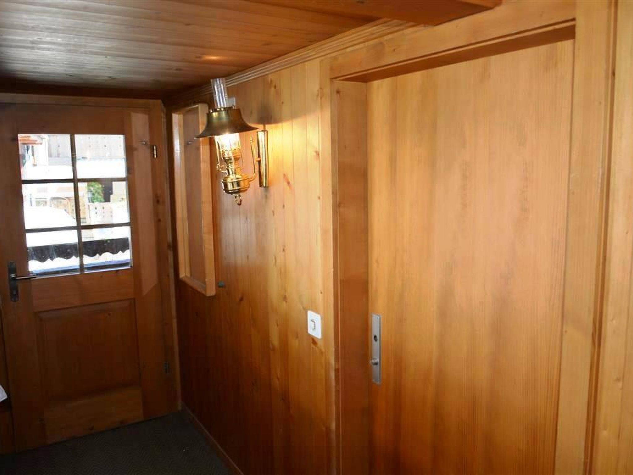 Un pasillo de madera con una puerta, un ventanal y una lámpara fijada a la pared.