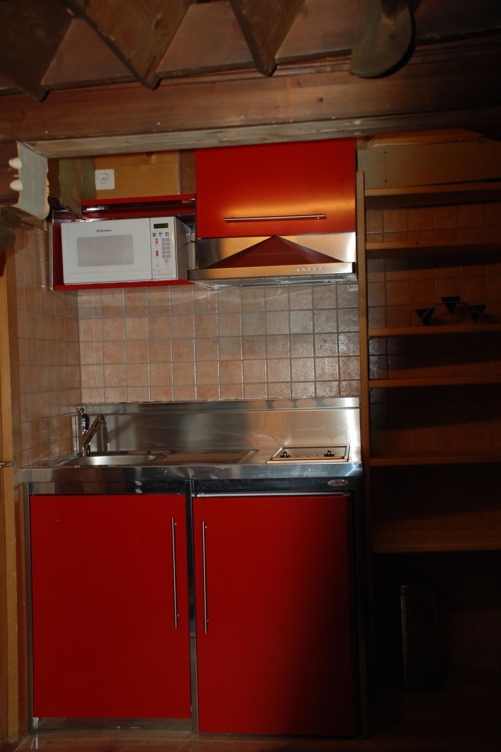 A compact kitchen with a microwave, red cabinets, and a stainless steel sink.