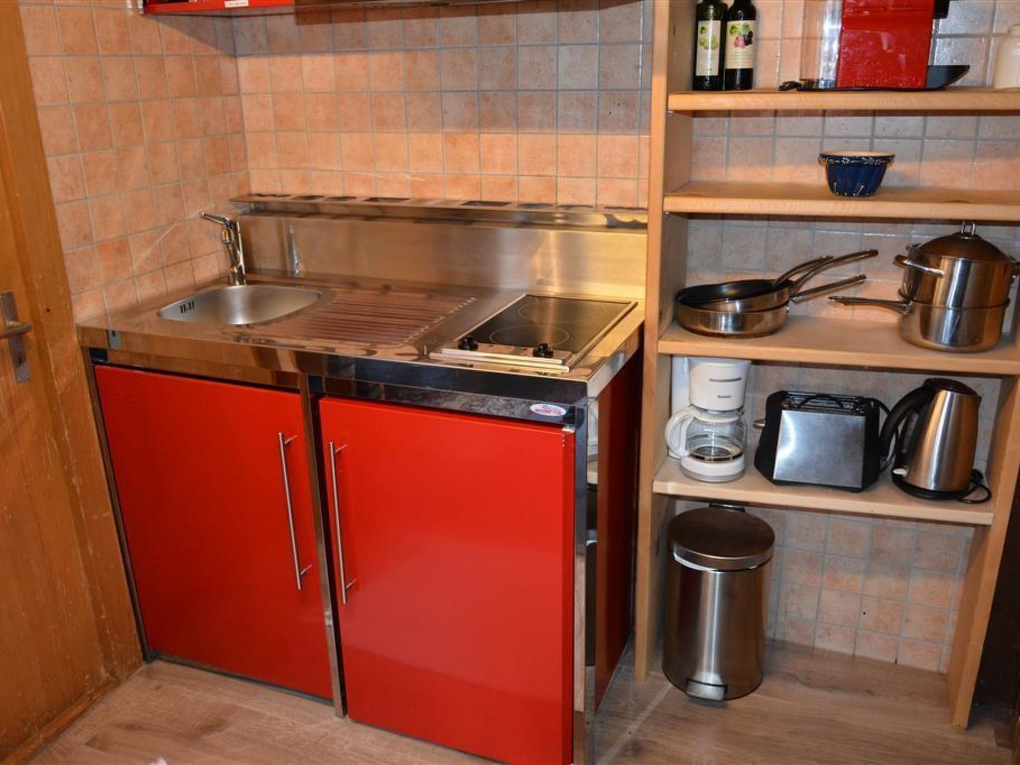 A compact kitchen with a red cabinet, a sink, a stove, and various kitchen utensils on shelves.