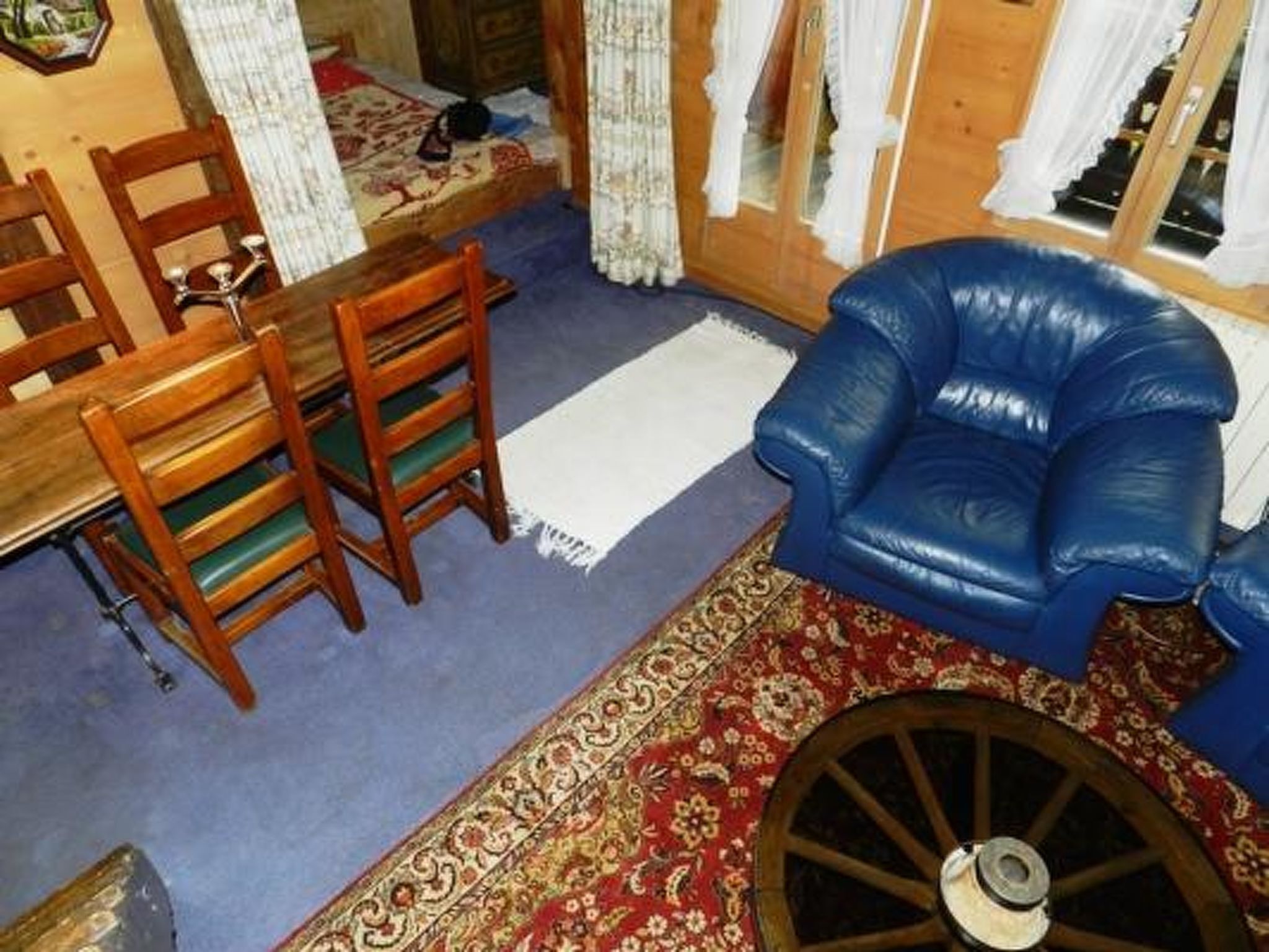 A room with a blue armchair, wooden chairs, a dining table, and a patterned rug.