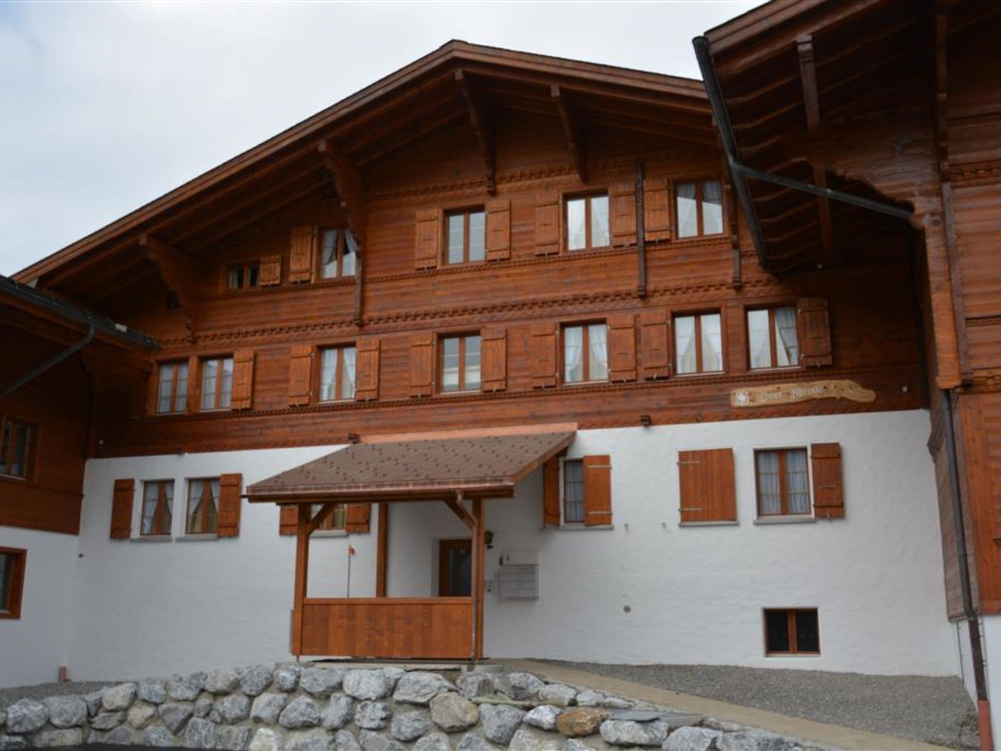 A multi-story wooden building with a stone foundation, wooden shutters, and a central entrance with a roofed porch.