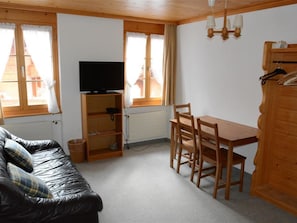 A room with a black leather sofa, a wooden dining table with chairs, a television on a shelf, and a window with curtains. - Mireille Nr. 3 Appartement/Fewo, Dusche oder Bad, WC 2-Bettwohnung by Interhome (Gstaad)