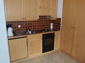 A compact kitchen with wooden cabinets, a black dishwasher, and a tiled backsplash. - Mireille Nr. 3 Appartement/Fewo, Dusche oder Bad, WC 2-Bettwohnung by Interhome (Gstaad)