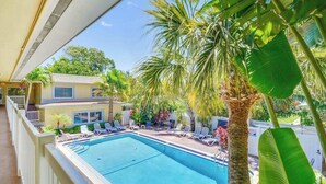 A pool with lounge chairs, a palm tree, and a building in the background. - Cozy Condo, Steps to St. Pete Beach + Shared Pool (St. Petersburg Beach)