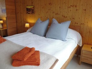 A wooden-paneled room with a bed, pillows, a nightstand, a lamp, and a painting on the wall. - Silberdistel Appartement/Fewo, Dusche, WC, 2 Schlafräume 4-Bettwohnung by Interhome (Lauenen b. Gstaad)