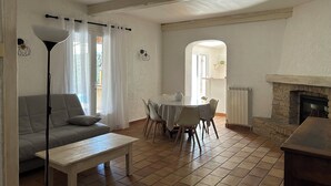 Ein Wohnzimmer mit einer Couch, einem Couchtisch, einem Esstisch mit Stühlen, einem Kamin und Blick durch einen Bogen in einen weiteren Raum.
