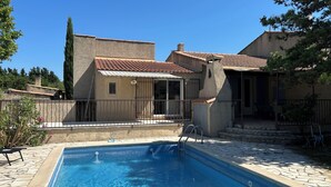 Ein Schwimmbecken mit einer Steindeck, einer überdachten Terrasse und einem Haus mit einem Ziegeldach.