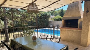 Eine Außenpatio mit Tisch und Stühlen, einer hängenden Leuchte, einem Steinofen und einem Pool im Hintergrund.