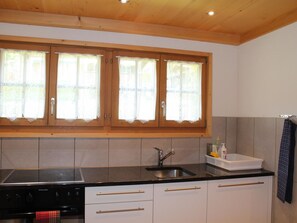 A kitchen with wooden cabinets, a black countertop, a sink, and a stove. - Beatrice Appartement/Fewo, Dusche oder Bad, WC 7-Bettwohnung by Interhome (Gstaad)