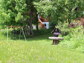 A garden with a swing set, a birdhouse, and a building in the background. - Beatrice Appartement/Fewo, Dusche oder Bad, WC 7-Bettwohnung by Interhome (Gstaad)