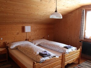 A wooden cabin bedroom with a double bed, a hanging light fixture, and a radiator. - Beatrice Appartement/Fewo, Dusche oder Bad, WC 7-Bettwohnung by Interhome (Gstaad)