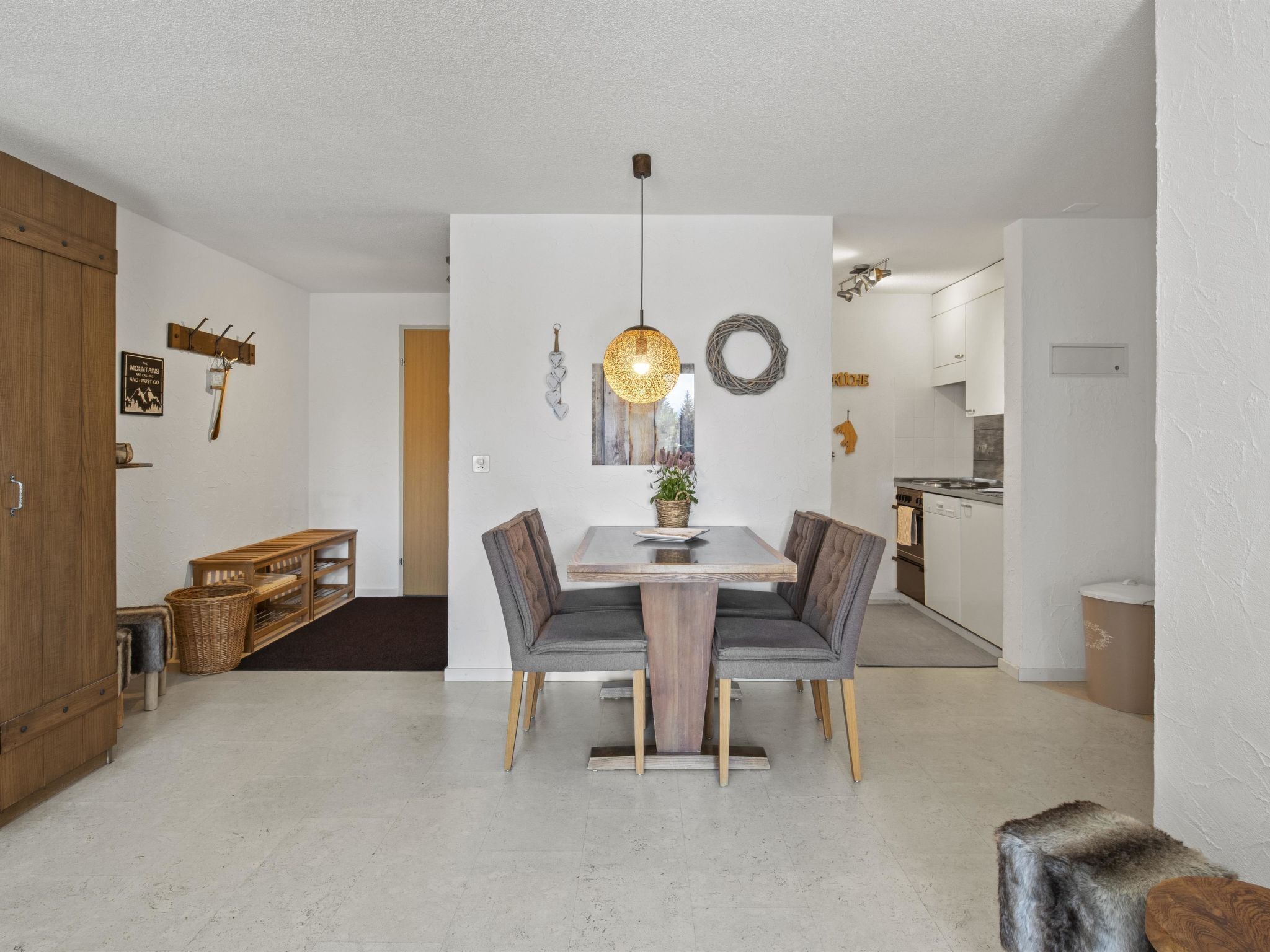 Een moderne eetruimte met een houten tafel en grijze gestoffeerde stoelen, een hanglamp en een keuken op de achtergrond.