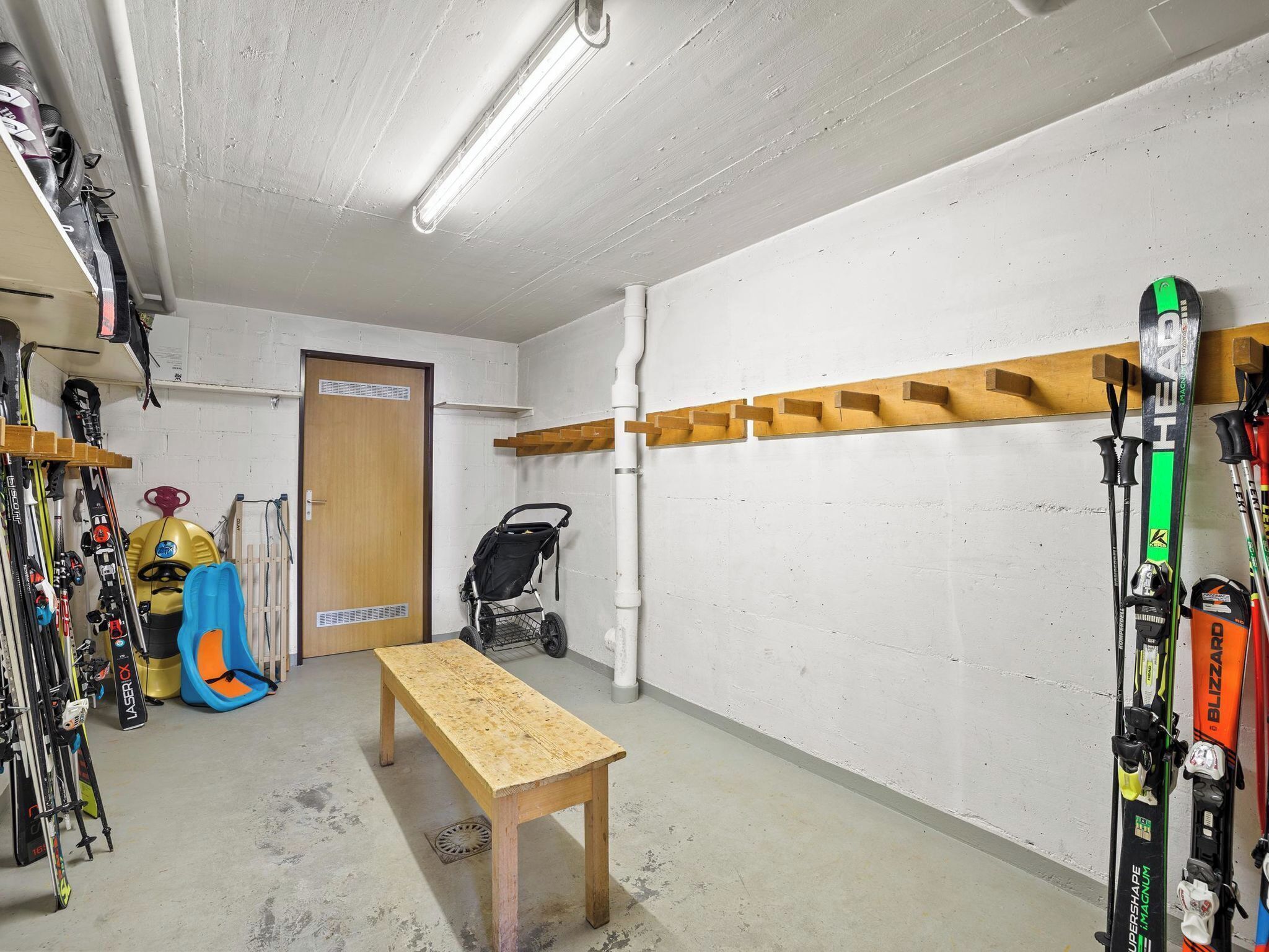 A ski storage room with a wooden bench, skis, and a stroller.