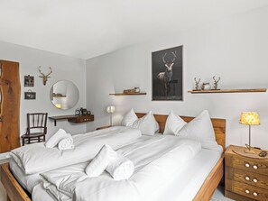 Ein modernes Schlafzimmer mit einem großen Bett, einem Holzstuhl, einem Nachttisch mit Lampe und Wandregalen mit Dekorationsobjekten.