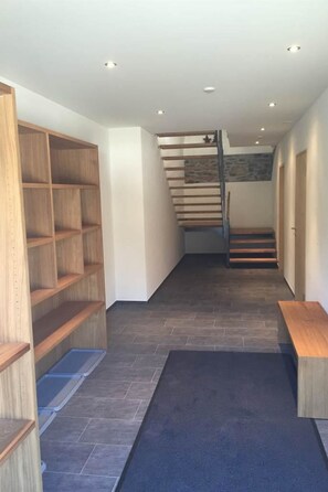 A hallway with a staircase leading to a landing, wooden shelving units, and a blue carpet. - Chesa Parpan Appartement/Fewo Appartement/Fewo by Interhome (Valbella)