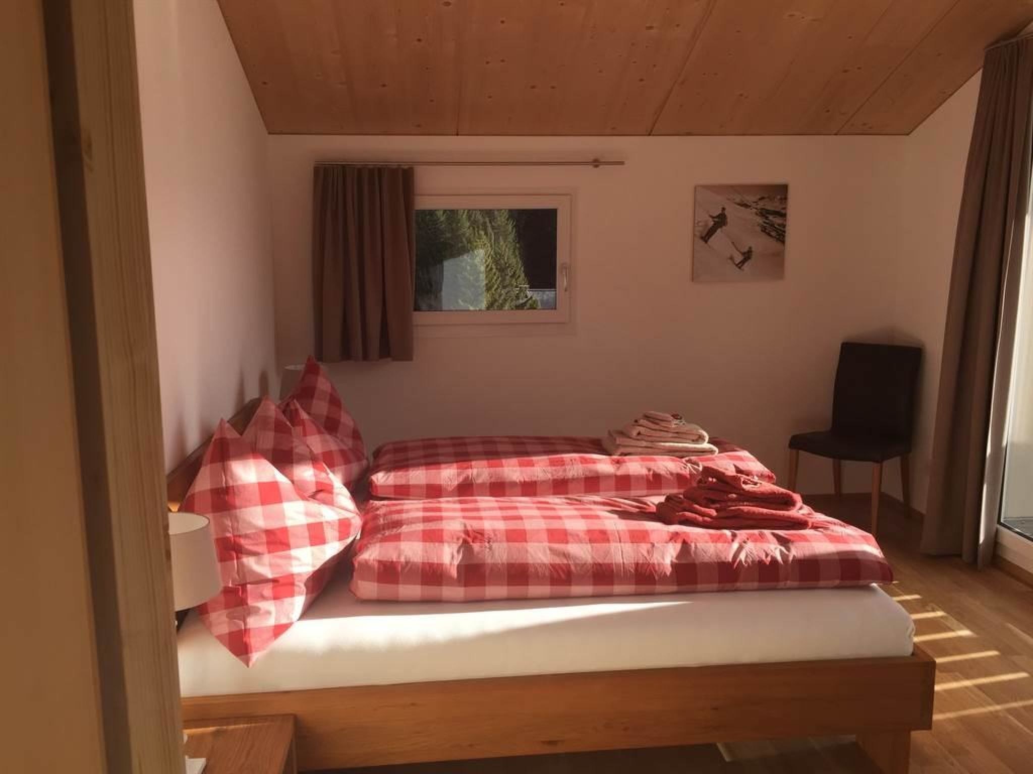 A bedroom with a wooden bed, checkered bedding, a window with a view, and a chair.