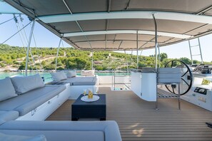 Ein Yachthausdeck mit überdachter Sitzecke, einer Steuerung und Blick auf die Küste.