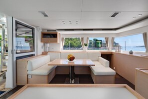 Ein modernes Interieur mit einem zentralen Tisch, gepolsterten Sitzgelegenheiten und großen Fenstern mit Meerblick.