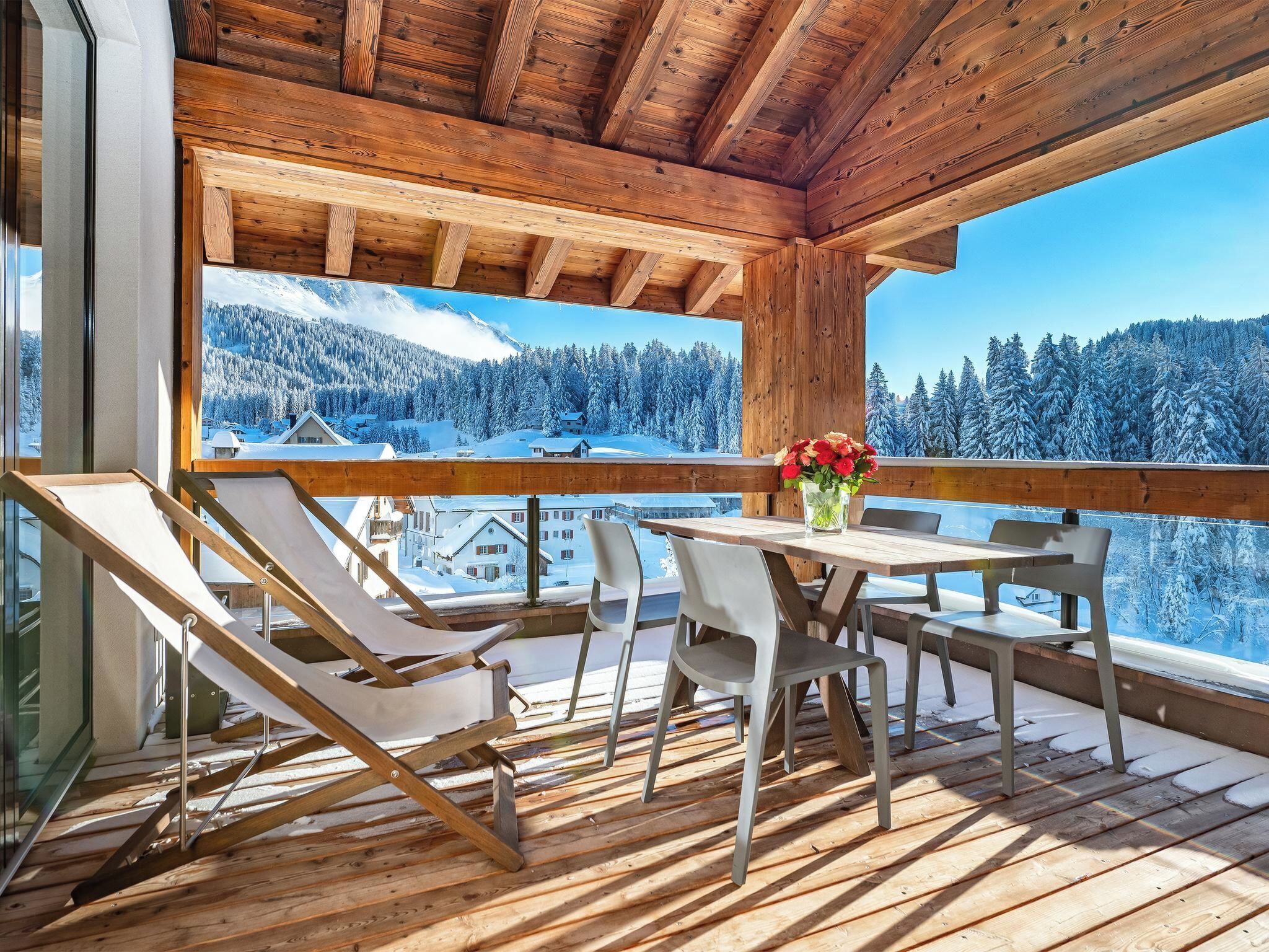 Una terraza de madera con una mesa y sillas, con vistas a un paisaje montañoso nevado.
