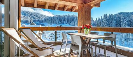 A wooden deck with a table and chairs, overlooking a snowy mountain landscape.