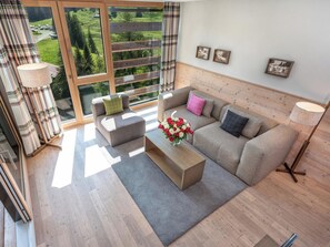 Una sala de estar moderna con un sofá, una mesa de centro y vistas a un paisaje verde a través de amplios ventanales.