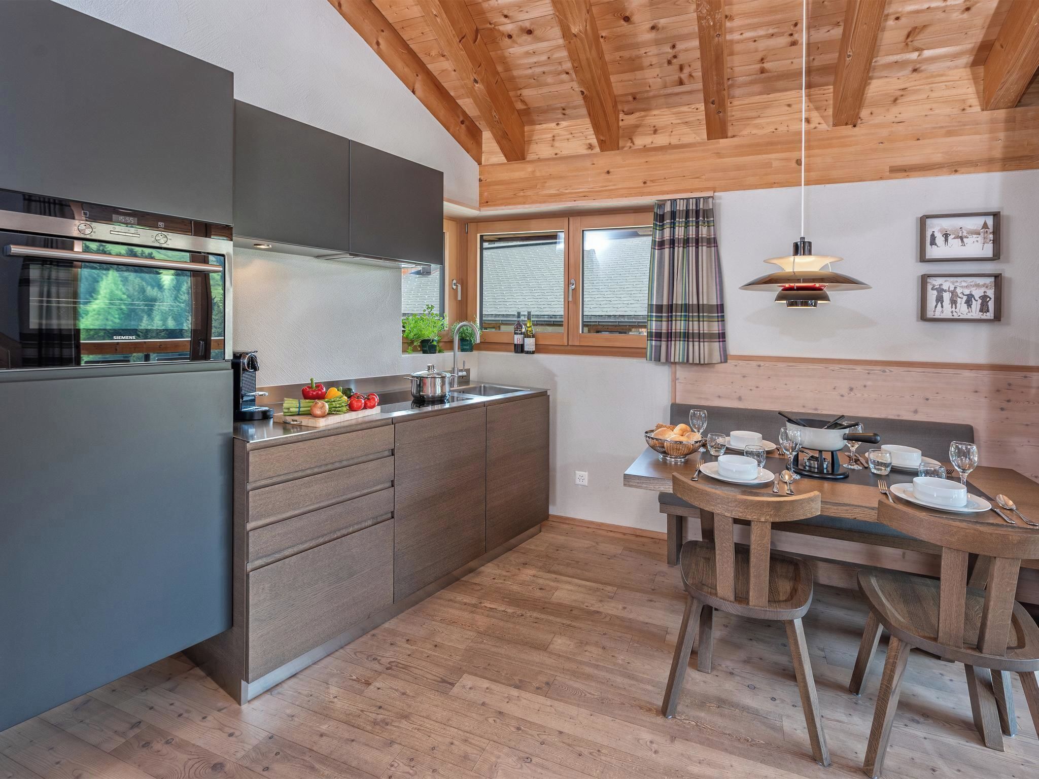 A modern kitchen with a built-in oven, a dining area with a wooden table and chairs, and a view of the outdoors through large windows.