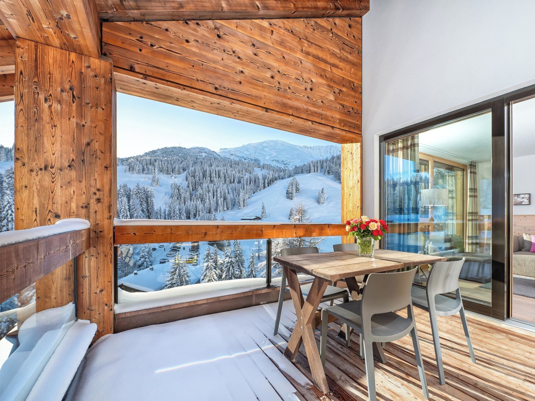 Ein Holzbalkon mit Tisch und Stühlen, mit Blick auf eine verschneite Berglandschaft.