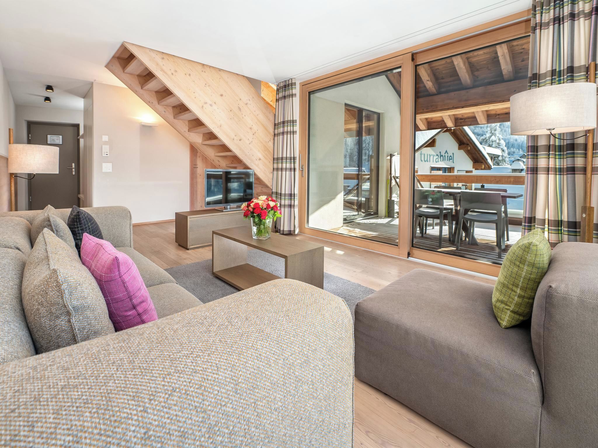 A modern living room with a sofa, a coffee table, and a TV. There is a staircase leading to an upper level.
