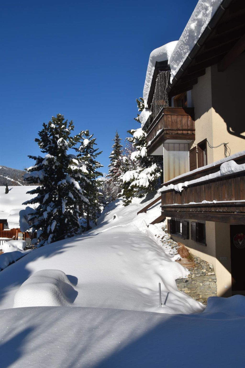 Un bâtiment recouvert de neige, doté d’une façade en bois et de fondations en pierre, entouré d’arbres chargés de neige.