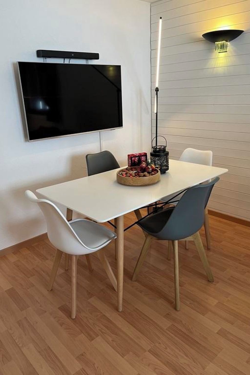 A dining area with a flat-screen TV mounted on the wall, a table with chairs, and a floor lamp.