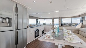 Una cucina moderna con elettrodomestici in acciaio inossidabile, una zona pranzo con tavolo imbandito per quattro persone e vista sul mare attraverso ampie finestre.