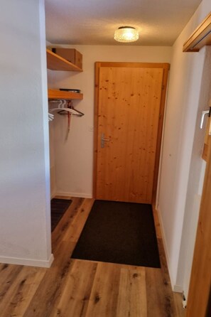 A narrow hallway with a wooden door, a black mat at the entrance, and a wooden shelf with a white towel. - Haus Sunneschy Whg. 202 Appartement/Fewo, Dusche, WC 2.5  Zimmerwohnung/ Whg.202 by Interhome (Parpan)