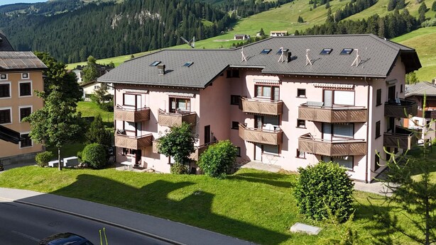 Ein mehrstöckiges Gebäude mit Balkonen, umgeben von üppigen grünen Hügeln und Bergen.