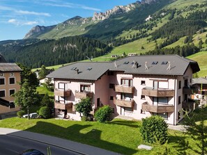 Ein mehrstöckiges Gebäude mit Balkonen, umgeben von üppigen grünen Hügeln und Bergen.