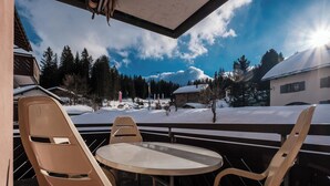 Ein überdachter Außenbereich mit Tisch und Stühlen, mit Blick auf eine verschneite Landschaft mit Bäumen und Gebäuden.