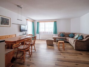 A living room with a wooden dining table, chairs, a sofa, and a television. - Haus Sunneschy Whg. 202 Appartement/Fewo, Dusche, WC 2.5  Zimmerwohnung/ Whg.202 by Interhome (Parpan)