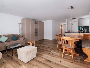 Ett modernt vardagsrum med soffa, pall, matbord, stolar och ett köksområde.