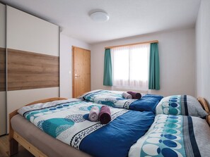 Ein Schlafzimmer mit einem Bett, einem Kleiderschrank, einem Fenster mit Vorhängen und einer Deckenleuchte.