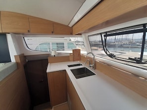 A compact galley with a sink, a window with a view of boats, and wooden cabinetry. - Sun-Kissed Sailing Adventure in the Ionian Islands, Lefkada (Lefkada)