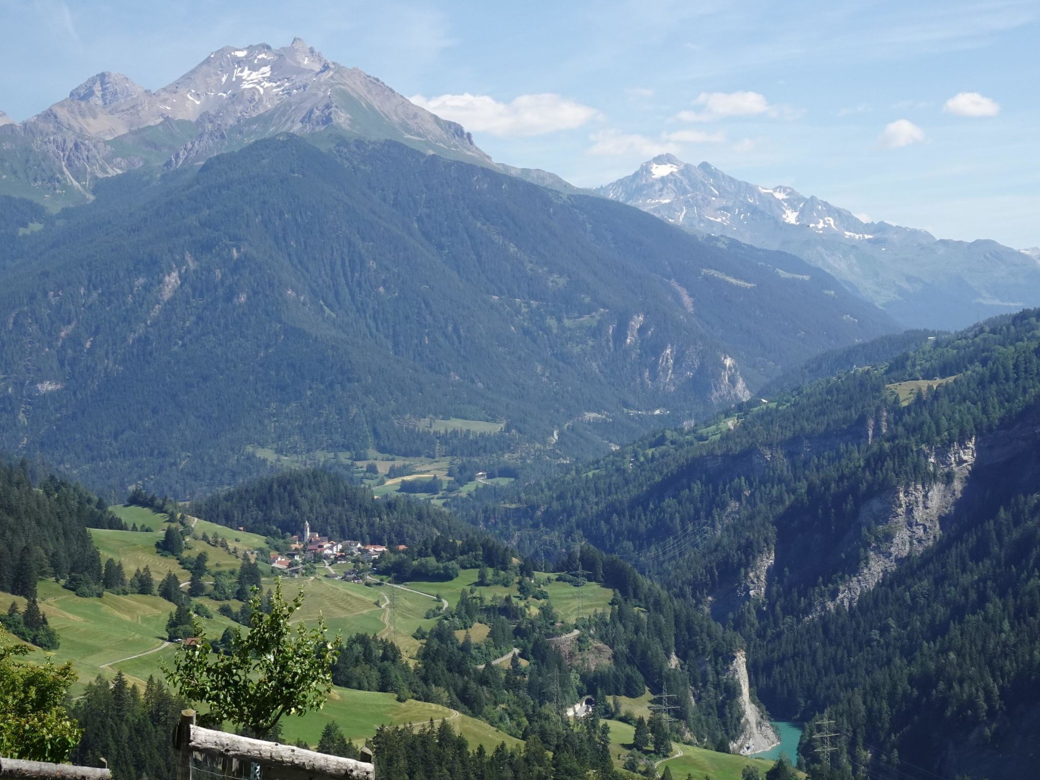 Un paisaje montañoso con un valle, un pequeño asentamiento y un lago.