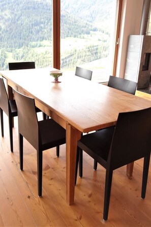 A dining table with six chairs, a bowl of fruit, and a view of a forest through large windows. - Pas-Cheus Appartement/Fewo, Bad, WC, 2 Schlafräume by Interhome (Vaz)