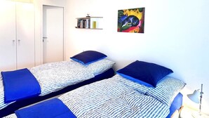 Quarto com duas camas de solteiro, uma estante, um quadro e um abajur.