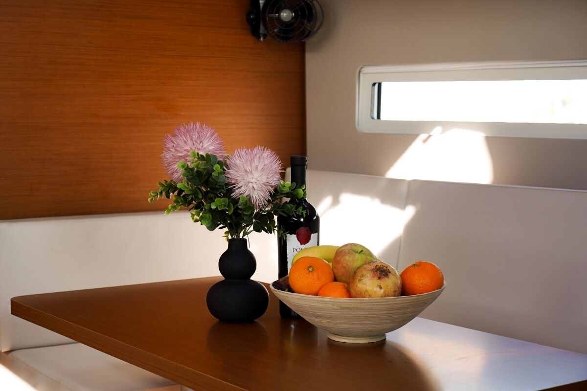 A wooden table with a vase of flowers and a bowl of fruit.