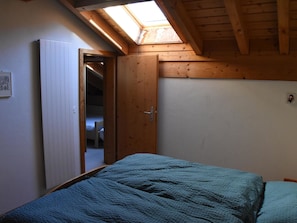 Ein Schlafzimmer mit Oberlicht, einem Bett mit blauer Decke und einer Holztür zu einem Badezimmer.