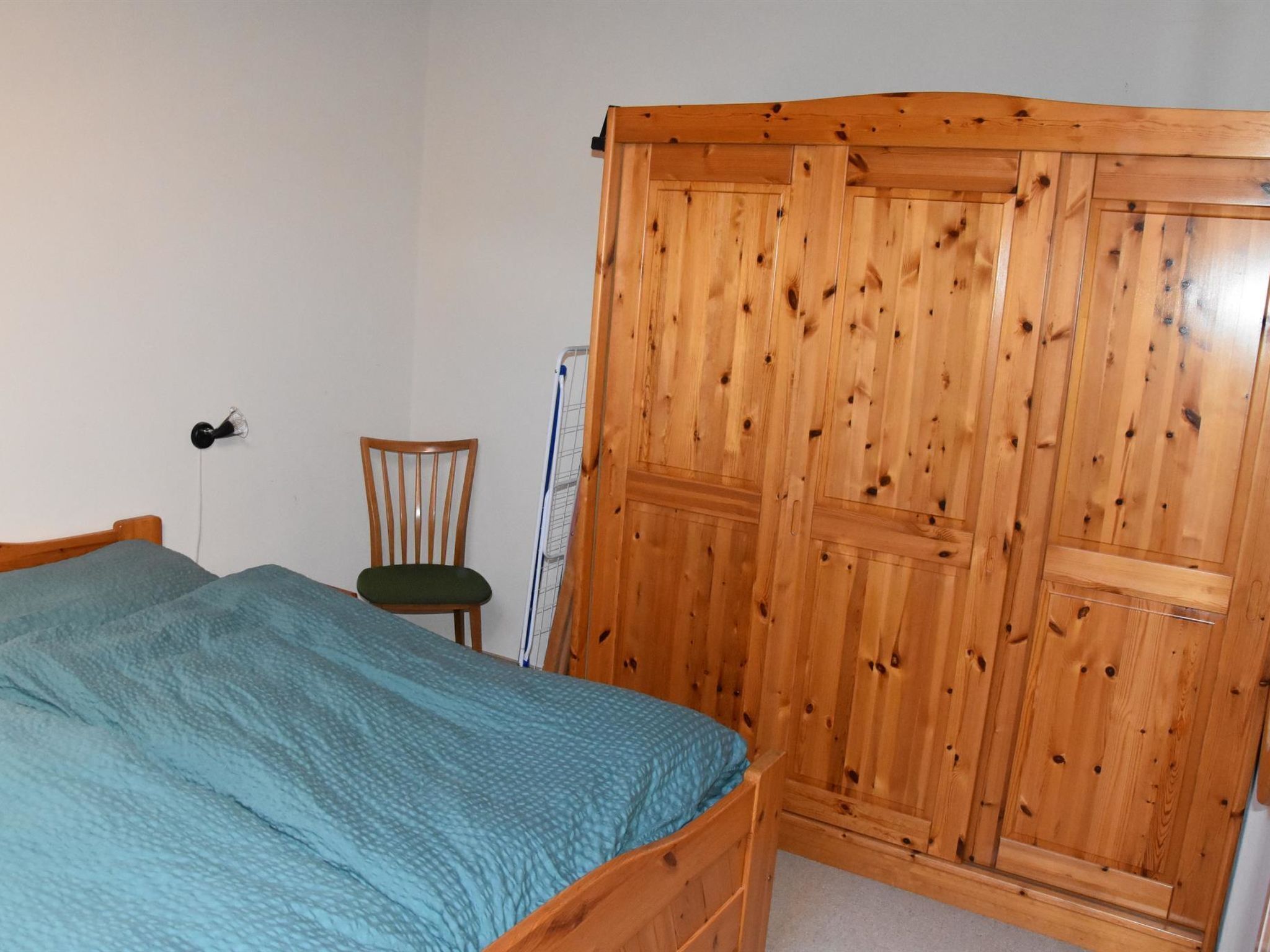 A bedroom with a bed, a wooden wardrobe, and a chair.