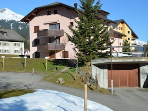 Ein mehrstöckiges Gebäude mit Balkonen, verschneitem Gelände und einem Berg im Hintergrund.