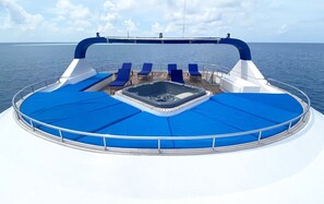 Ein Bootsdeck mit Whirlpool, Liegestühlen und Blick auf den Ozean.